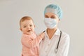 Portrait of excited kid and young adult female pediatrist wearing medical uniform, woman holding infant baby girl, examining child