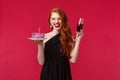 Portrait of excited laughing gorgeous redhead woman having fun at b-day party, holding glass of wine and birthday cake Royalty Free Stock Photo