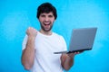 Portrait of an excited man holding laptop computer and celebrating success isolated over blue background Royalty Free Stock Photo