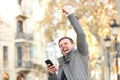 Excited man holding phone and raising arm in the street Royalty Free Stock Photo