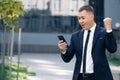 Portrait of excited man reading good news at smartphone outdoors. Successful businessman celebrating win with mobile Royalty Free Stock Photo