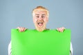 Portrait of excited man showing blank signboard with copyspace area for slogan or text. Young funny man shows a sheet of