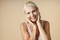 Portrait of excited mature woman with blonde hair in white underwear smiling at camera, touching her face isolated over Royalty Free Stock Photo