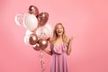 Portrait of excited young lady with bunch of balloons for birthday or Woman`s Day, celerating holiday on pink background