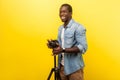 Portrait of excited motivated photographer posing professional digital dslr camera on tripod. studio shot isolated on yellow Royalty Free Stock Photo