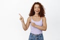Portrait of excited redhead girl showing announcement, pointing finger left at sale, banner, smiling amazed Royalty Free Stock Photo