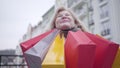 Portrait of excited senior Caucasian woman enjoying shopaholism outdoors. Focus changes from face to shopping bags and