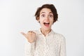 Portrait of excited smiling woman with short hair, wearing blouse, looking interested and amazed and pointing left Royalty Free Stock Photo