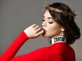 Sexy brunette woman with closed eyes and golden crown of thorns on her head in red turtleneck sweater biting her finger Royalty Free Stock Photo