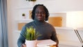 Portrait of excited young african american man moving in to the new apartment. Holding cardboard boxes with plant and Royalty Free Stock Photo