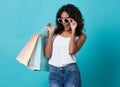 Portrait of an excited young african woman hand holding shopping bag and sunglasses isolated over blue background Royalty Free Stock Photo