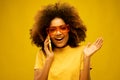 Portrait of an excited young afro american woman talking on mobile phone while standing isolated over yellow background Royalty Free Stock Photo