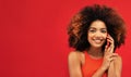 Portrait of an excited young afro american woman talking on mobile phone while standing over red color background Royalty Free Stock Photo