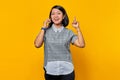 Portrait of excited young Asian woman holding smartphone with an idea or question pointing finger on yellow background Royalty Free Stock Photo