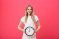 Portrait of an excited young girl dressed in white t-shirt pointing at alarm clock and looking at camera isolated over Royalty Free Stock Photo