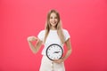 Portrait of an excited young girl dressed in white t-shirt pointing at alarm clock and looking at camera over Royalty Free Stock Photo