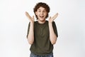 Portrait of excited young man with curly hair, looking fascinated and surprised, clap hands and cheer, standing over Royalty Free Stock Photo