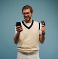 Portrait of an excited young man holding mobile phone and showing credit card isolated over blue background. Royalty Free Stock Photo