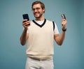 Portrait of an excited young man holding mobile phone and showing credit card isolated over blue background. Royalty Free Stock Photo