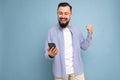 Portrait of an excited young man looking at mobile phone isolated over blue background, celebrating Royalty Free Stock Photo