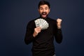 Portrait of an excited young man in ttrendy black sweater holding bunch of money banknotes and celebrating isolated over Pacific