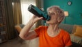 Portrait of an exhausted grayhaired elderly woman after a workout in the living room. Tired elderly woman drinks water