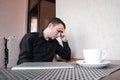 Portrait of exhausted worker in black shirt sleeping on his desktop in cafe with cup of coffee.