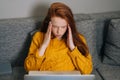 Portrait of exhausted young woman having headache while working typing on laptop computer sitting in sofa couch at home. Royalty Free Stock Photo