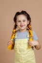 Portrait of exhilarated young girl holding yellow kanekalon pigtails with hands, smiling with missing tooth looking at Royalty Free Stock Photo
