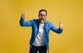 Portrait of exited businessman showing thumbs up and screaming in joy against yellow background