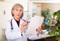 Elderly female doctor with papers studying clinical diagnosis of patient Royalty Free Stock Photo