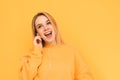 Portrait of an expressive blonde with headphones listening to music and rejoicing on a yellow background wearing an orange sweater