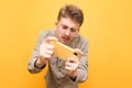 Portrait of expressive young man in glasses and shirt uses smartphone on yellow background, looks intently into the screen.