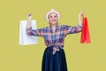 Happy cheerful mature woman in shirt, hat and eyeglasses, holding paper bags, enjoying shopping. Royalty Free Stock Photo