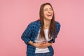 Portrait of extremely happy girl in checkered shirt holding her stomach and laughing out loud, chuckling giggling