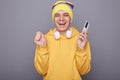 Portrait of extremely happy hipster man wearing casual clothing standing against gray wall, holding mobile phone and screaming Royalty Free Stock Photo