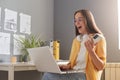 Portrait of extremely happy woman with brown hair wearing yellow shirt posing in office, looking at notebook display and screaming