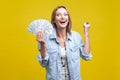 Portrait of extremely happy woman holding fan of dollars showing yes i did it gesture. on yellow background