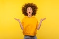 Portrait of extremely surprised girl in urban style hoodie jumping with her messy curly hair up, yellow background