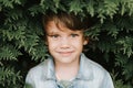 Portrait of the face of a cute little happy caucasian candid healthy five year old kid boy surrounded by branches and leaves of gr