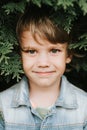 Portrait of the face of a cute little happy caucasian candid healthy five year old kid boy surrounded by branches and leaves of gr