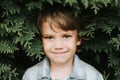 Portrait of the face of a cute little happy caucasian candid healthy five year old kid boy surrounded by branches and leaves of gr