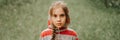 Portrait face of upset or focused thoughtful scowl eight year old kid girl in hood of striped hoodie in the forest or woodland nat