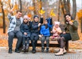 Portrait of a family with children in an autumn city park - happy people sitting together on a wooden bench, posing against a Royalty Free Stock Photo