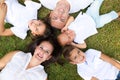 Portrait of a family of five, father, mother and children lying on the fresh grass looking at the camera. It is an example of a