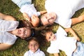 Portrait of a family of five, father, mother and children lying on the fresh grass looking at the camera. It is an example of a