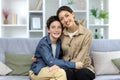 Portrait of family, mother and teenage son sitting on sofa at home and hugging, smiling at camera Royalty Free Stock Photo