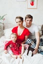 Portrait of family in pajamas sitting together in bed in decorated bedroom for Christmas and embracing.