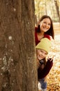 Portrait of family of young mother teenage girl standing behind tree among yellow fallen leaves, looking out of trunk. Royalty Free Stock Photo