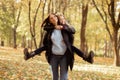 Portrait of family of young woman and teenage girl walking in forest. Mother giving piggyback ride to daughter. Autumn.